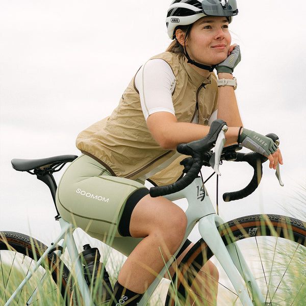 Cyclist leaning on her bike in a SOOMOM gilet and sage bib shorts